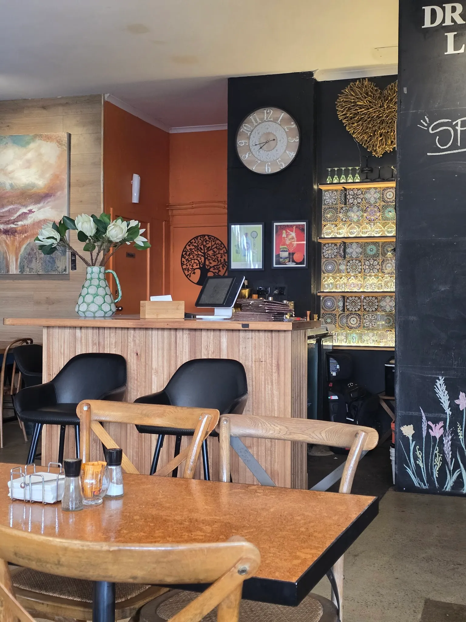 Cafe counter area with timber veneer, white flowers, wall clock, and decorative metal tree art