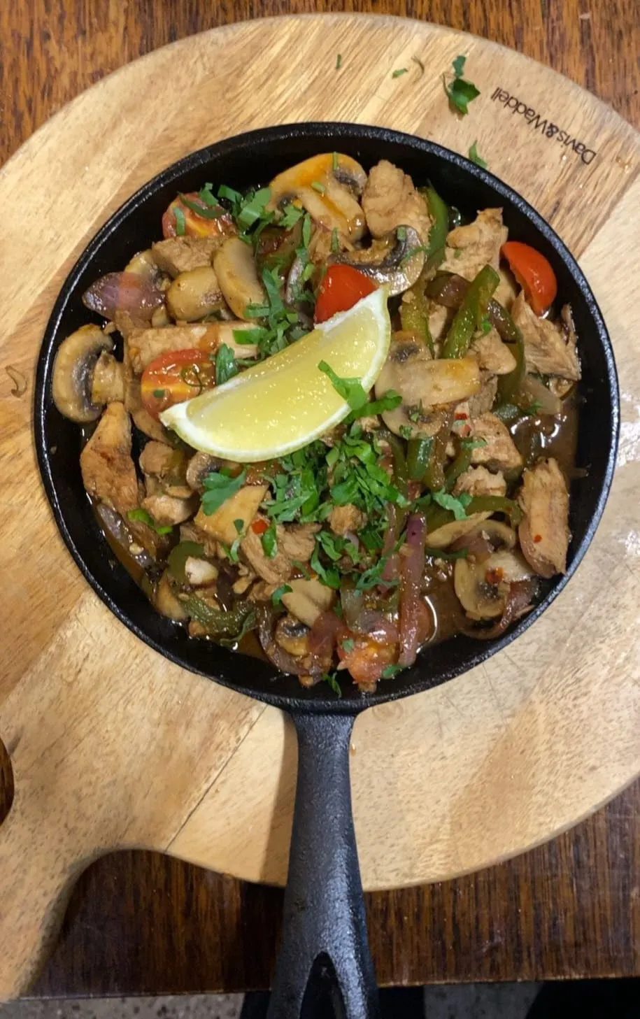 Cast-iron skillet with sauteed chicken, mushrooms, capsicum, and lime on a wooden board