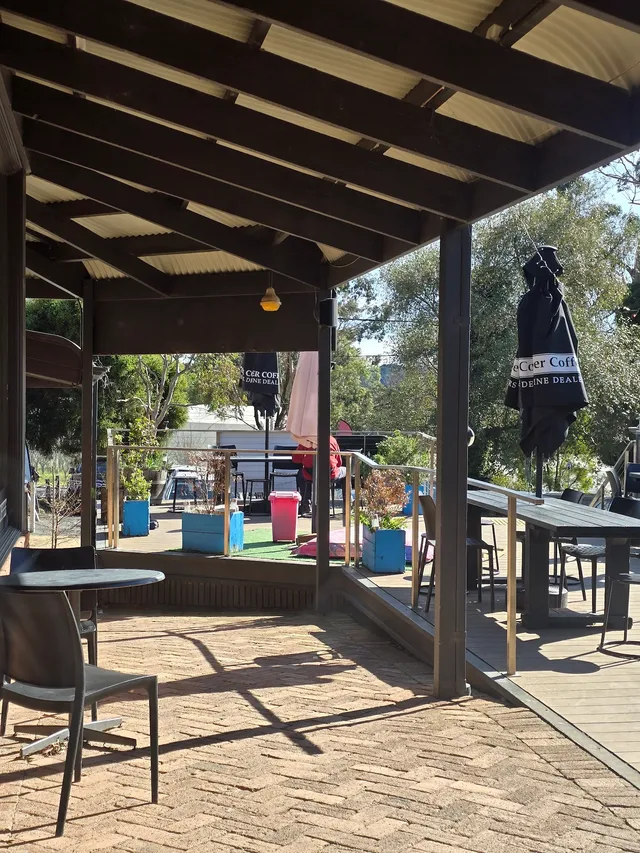 Outdoor alfresco deck at Red Hill Cafe, viewed from under corrugated iron pergola with timber tables and sunny garden beyond