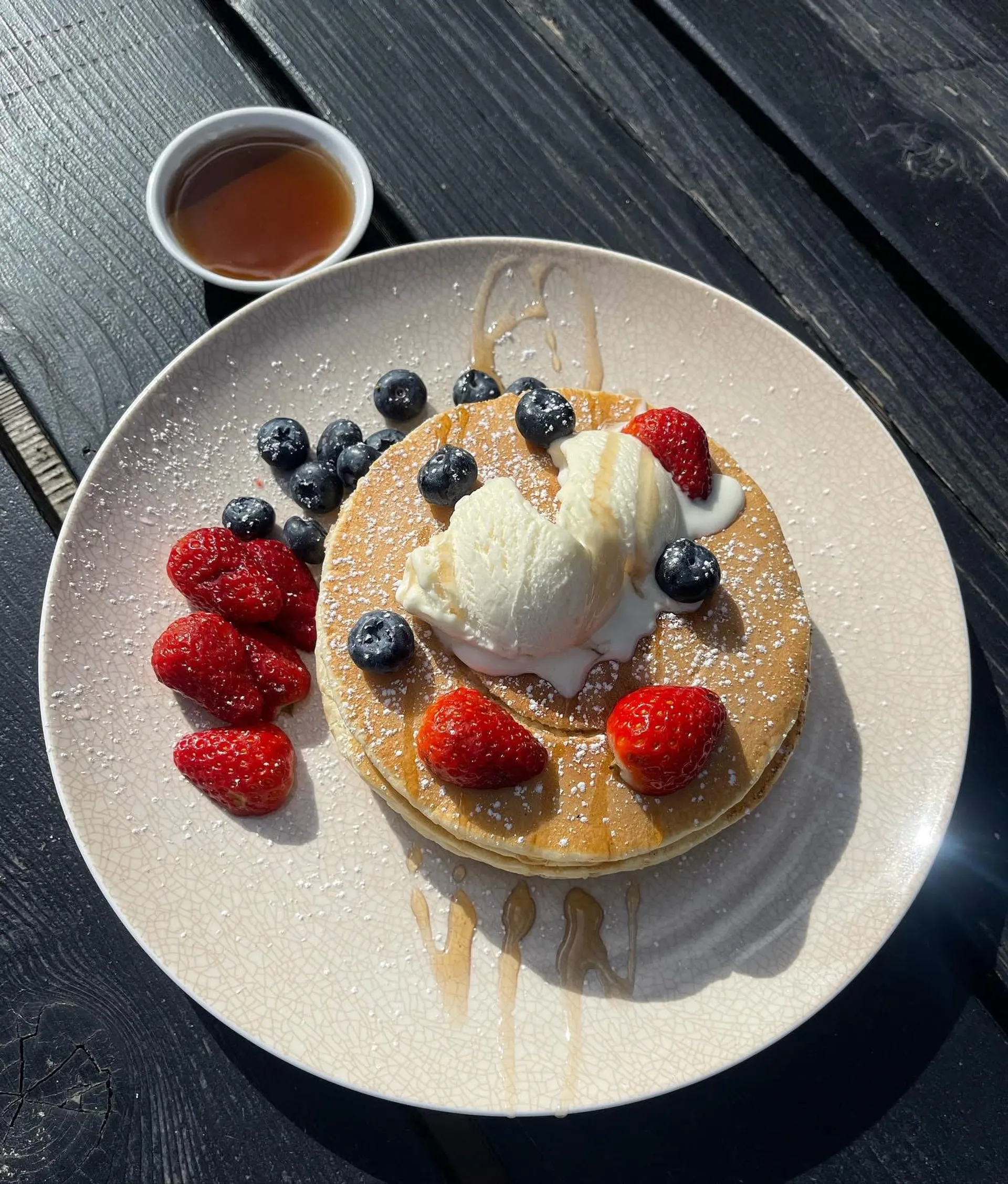 Fluffy pancakes topped with ice cream, fresh strawberries, blueberries and honey on a white plate