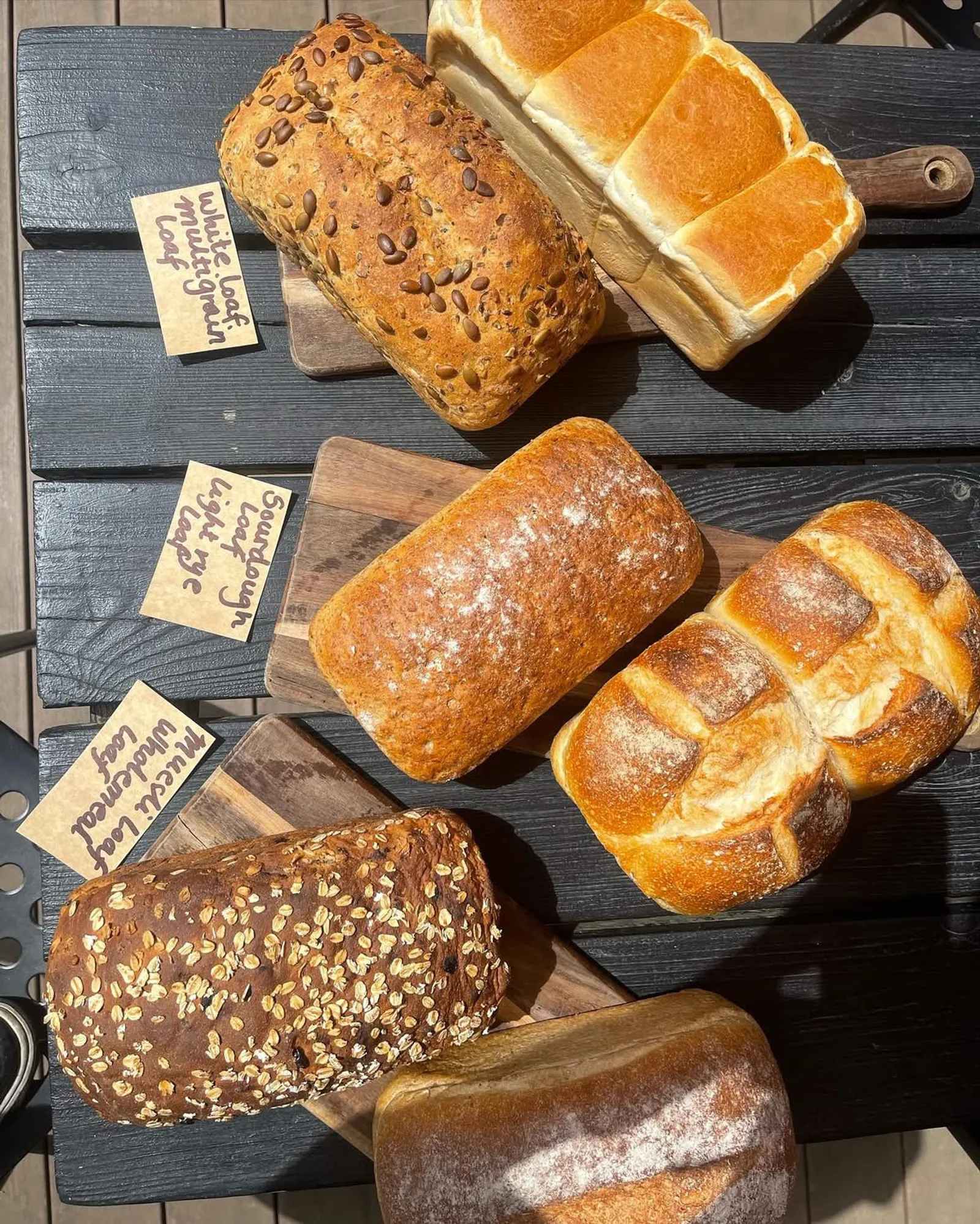 Five artisan bread loaves arranged on a dark wooden board with handwritten name labels