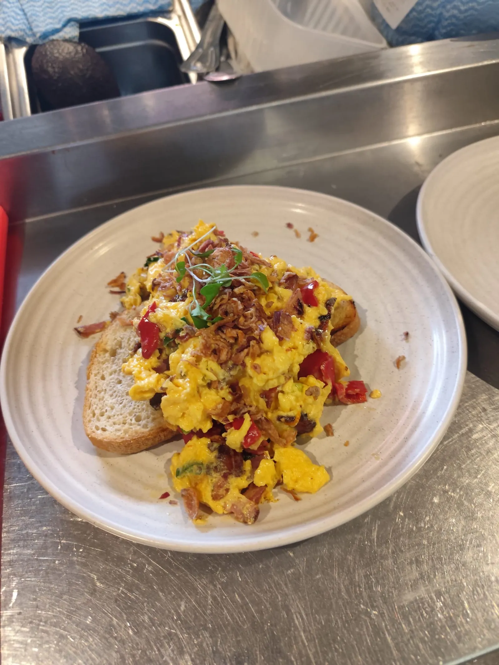 Chilli scrambled eggs on toast with microgreens and crispy shallots, photographed in a kitchen setting