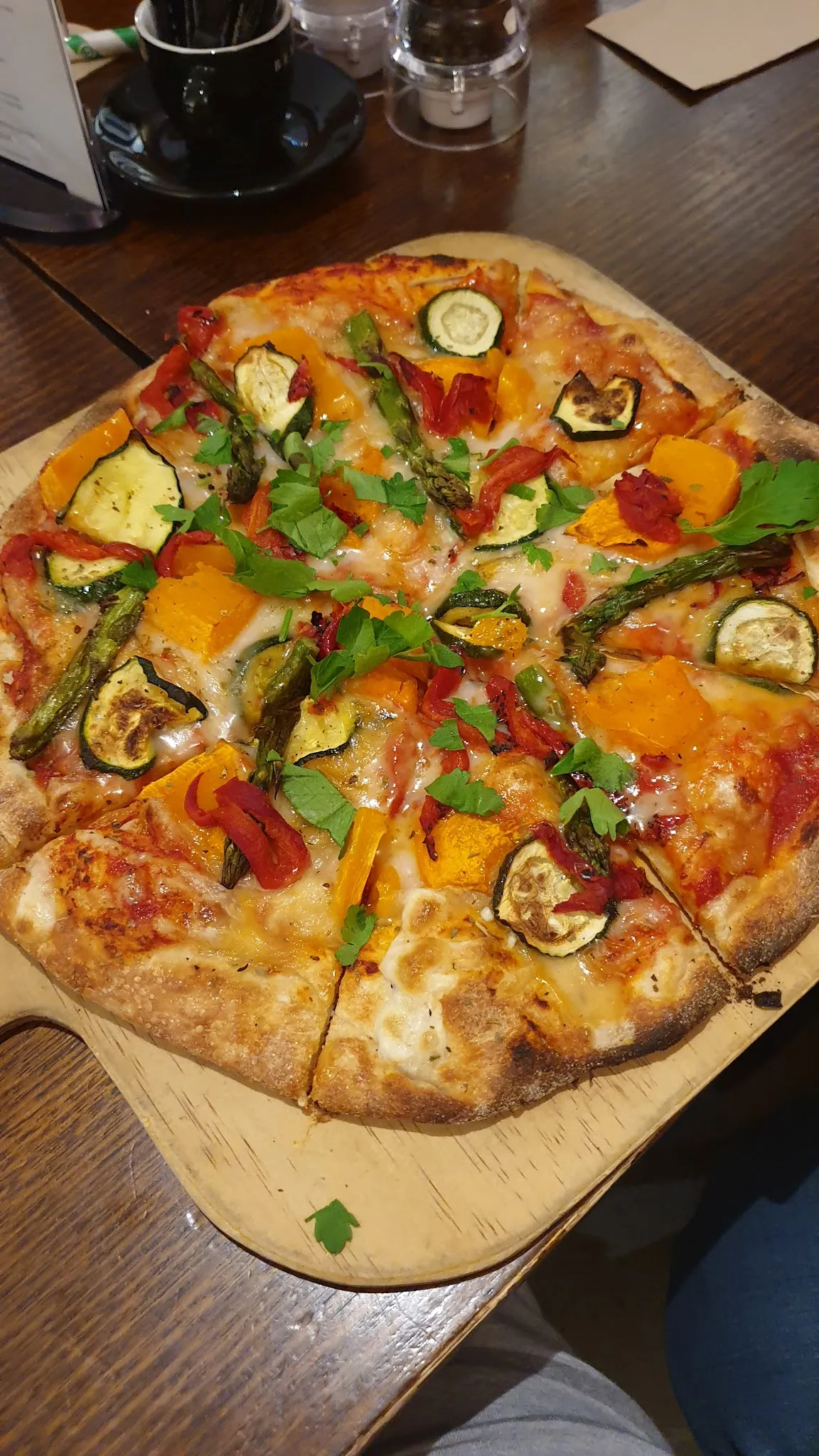 Whole vegetarian pizza on a wooden paddle board topped with roasted zucchini, pumpkin, asparagus and capsicum