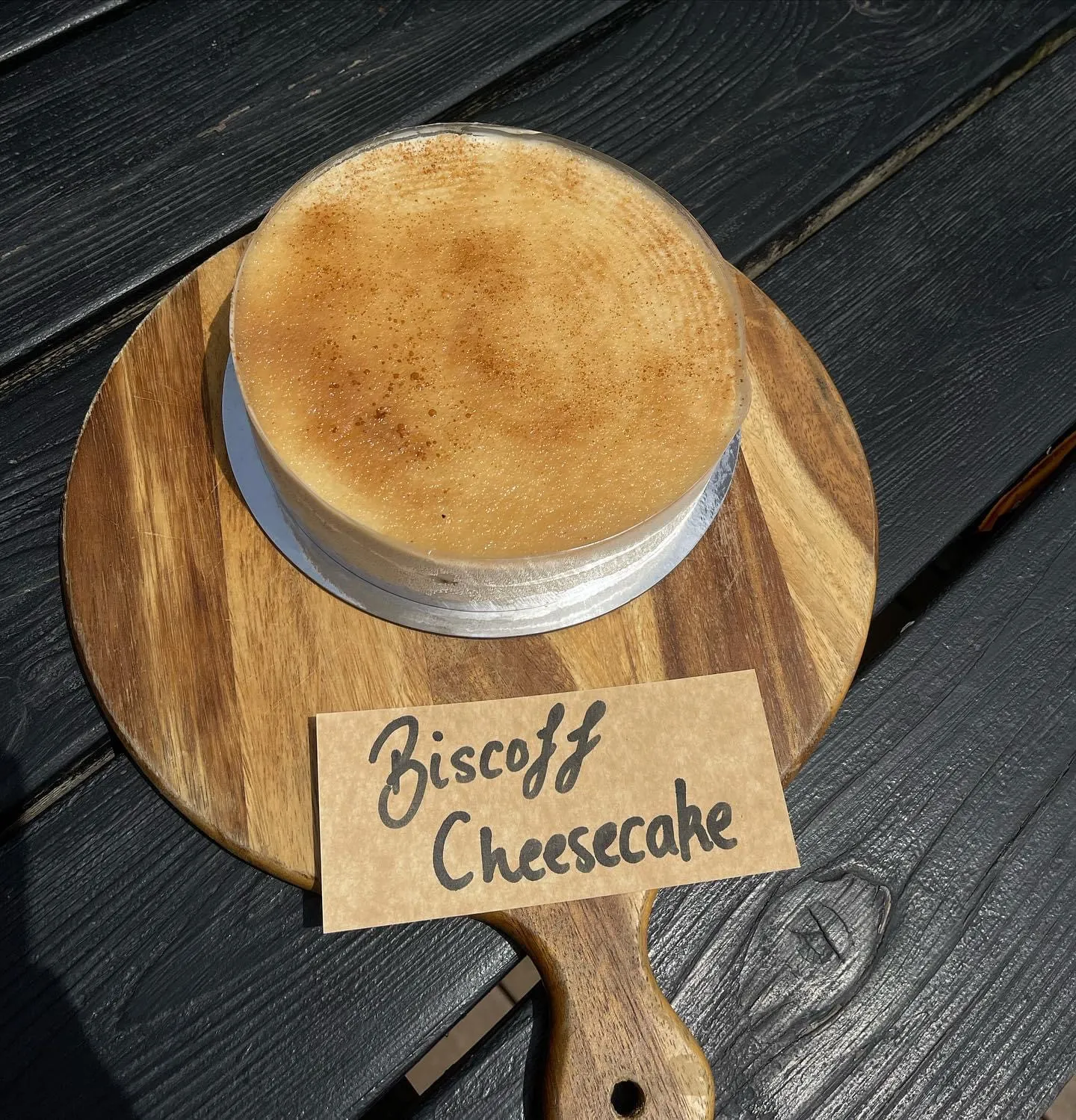 Whole Biscoff cheesecake in springform tin on a timber board with handwritten label