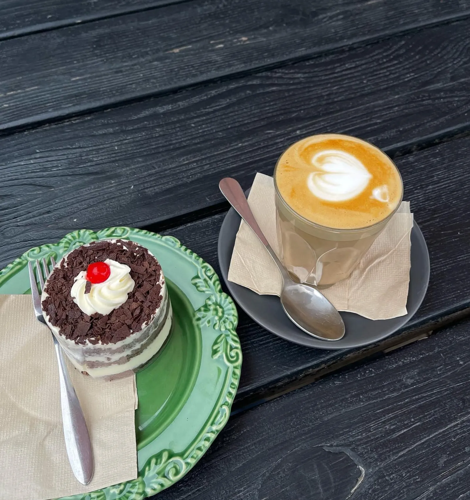Black Forest mini-cake on a green plate with a flat white coffee with latte art on a dark timber table